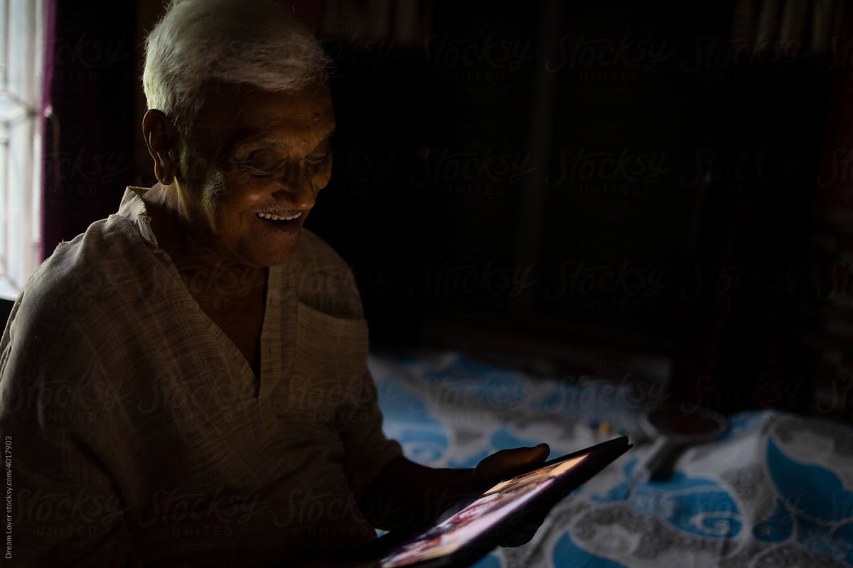 Aged Indian man sit on bed and watching movie in Tablet