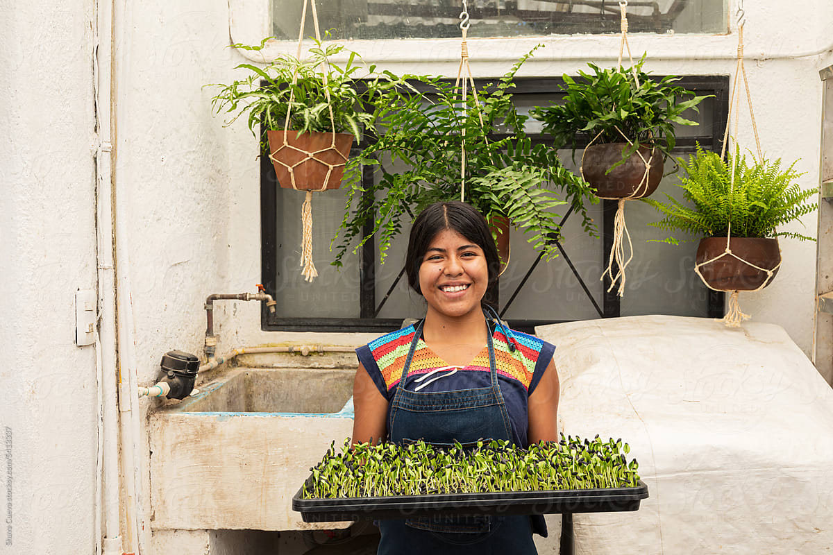 A smiling woman holding a tray of sunflower microgreens sprouts
