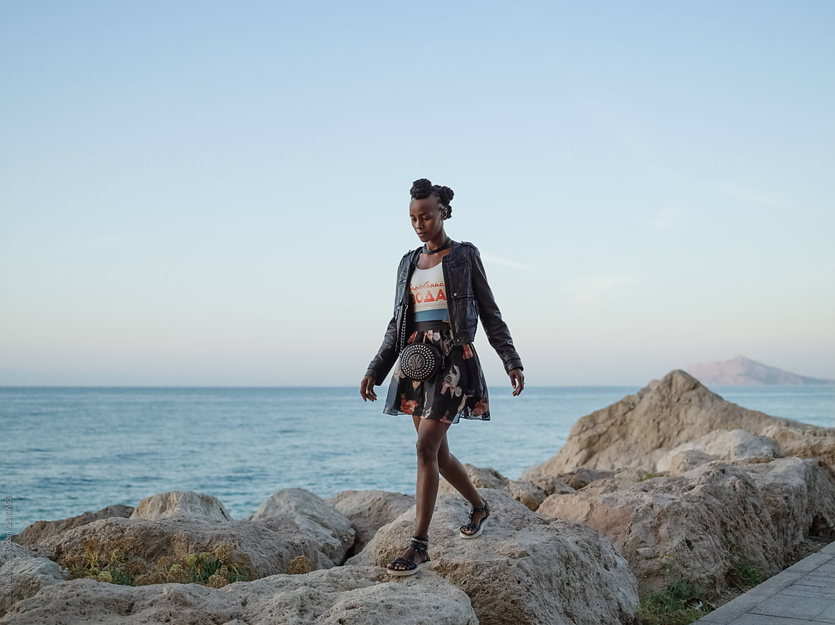 Black woman strolling on stones near sea