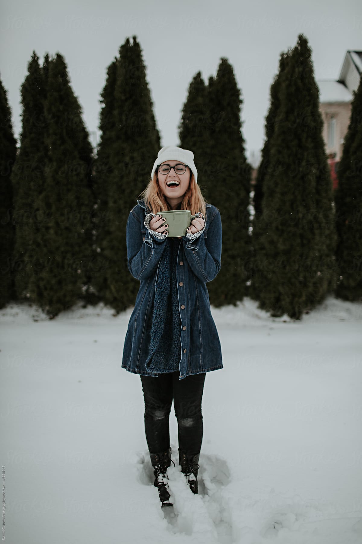 Lifestyle photo of a girl drinking from a large mug outdoors in the snow in front of trees in the winter