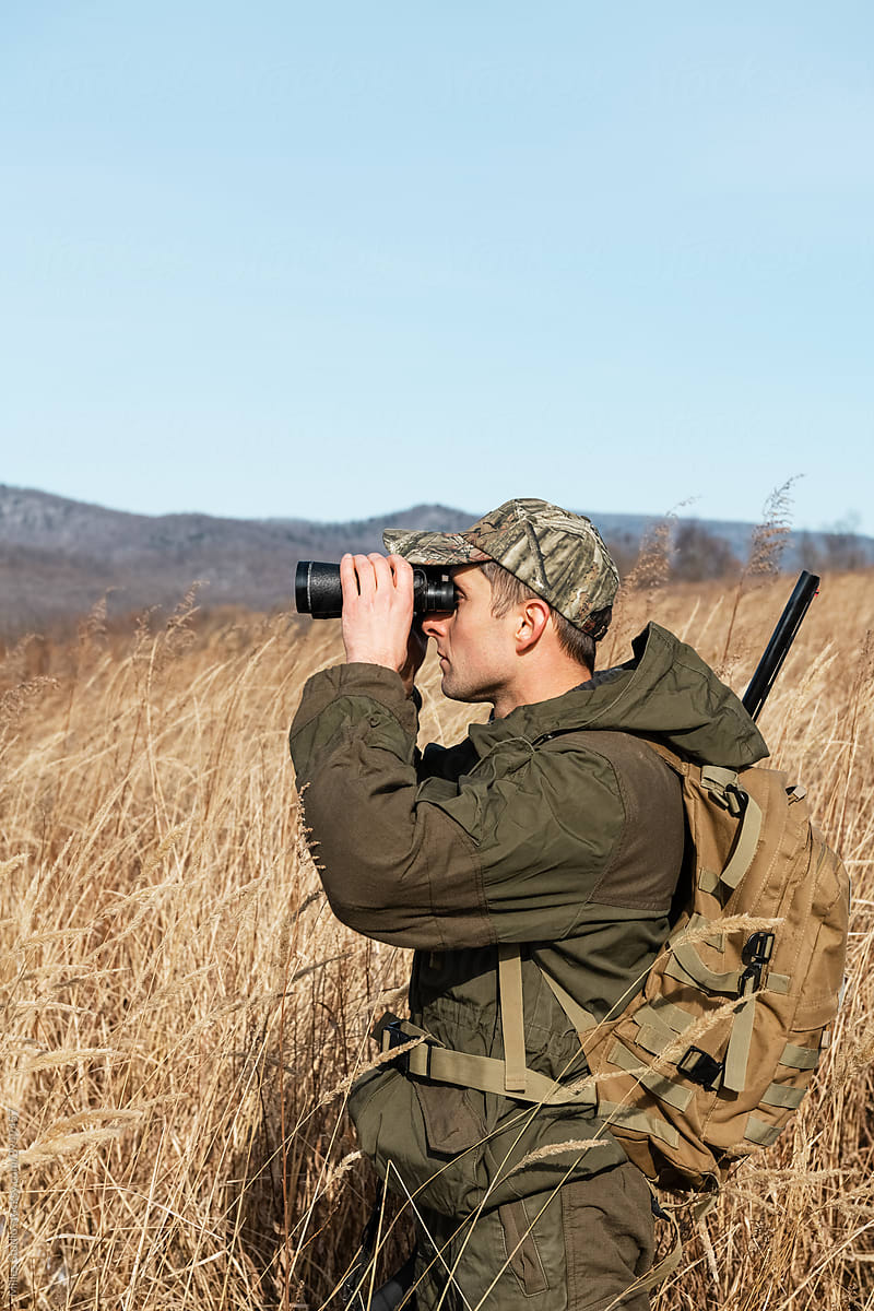 Male hunter using binoculars in dried grassy meadow