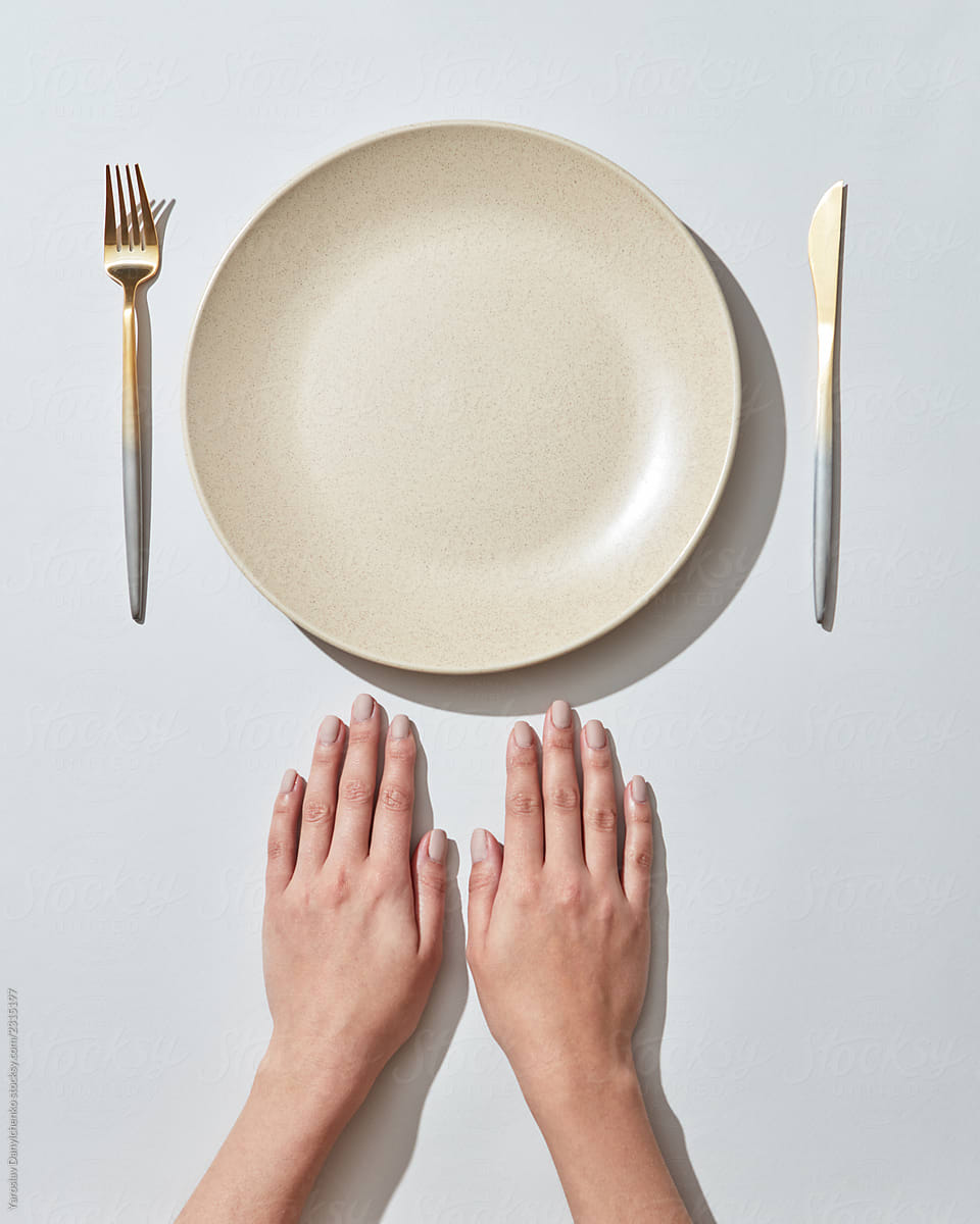 Empty plate, fork and knife with women's hands on a white background, copy space. Flat lay