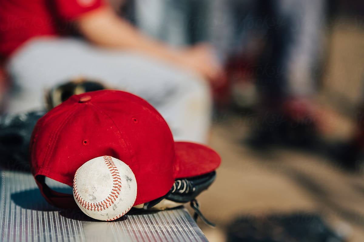 Red baseball cap and ball on a bench