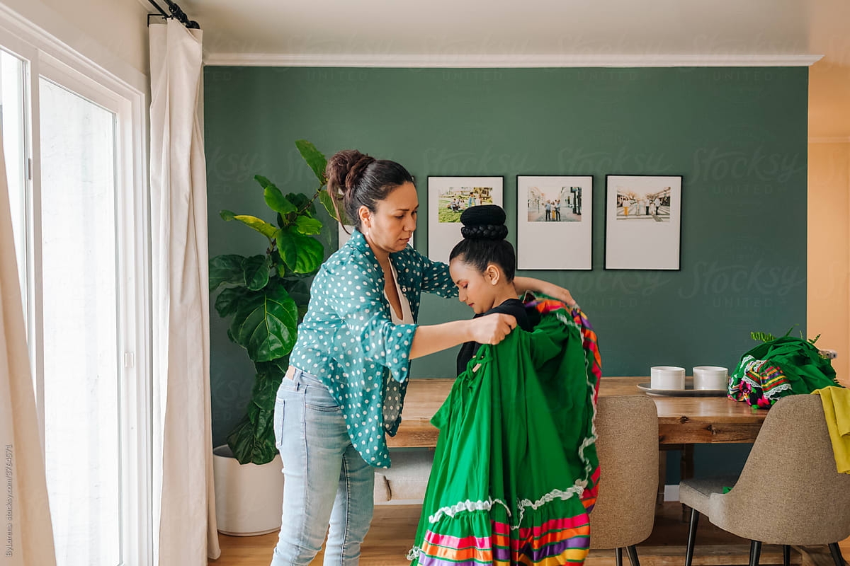 Mother helping daughter to dress up for a traditional Mexican perfomance