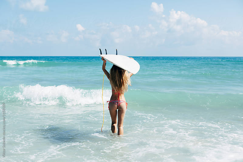 Sexy young beautiful woman carrying surfboard on hear head in the ocean ready to swim