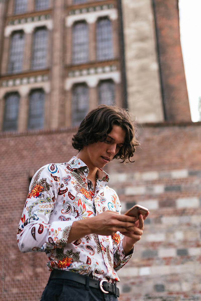 Young man wearing a colorful shirt is texting on the street