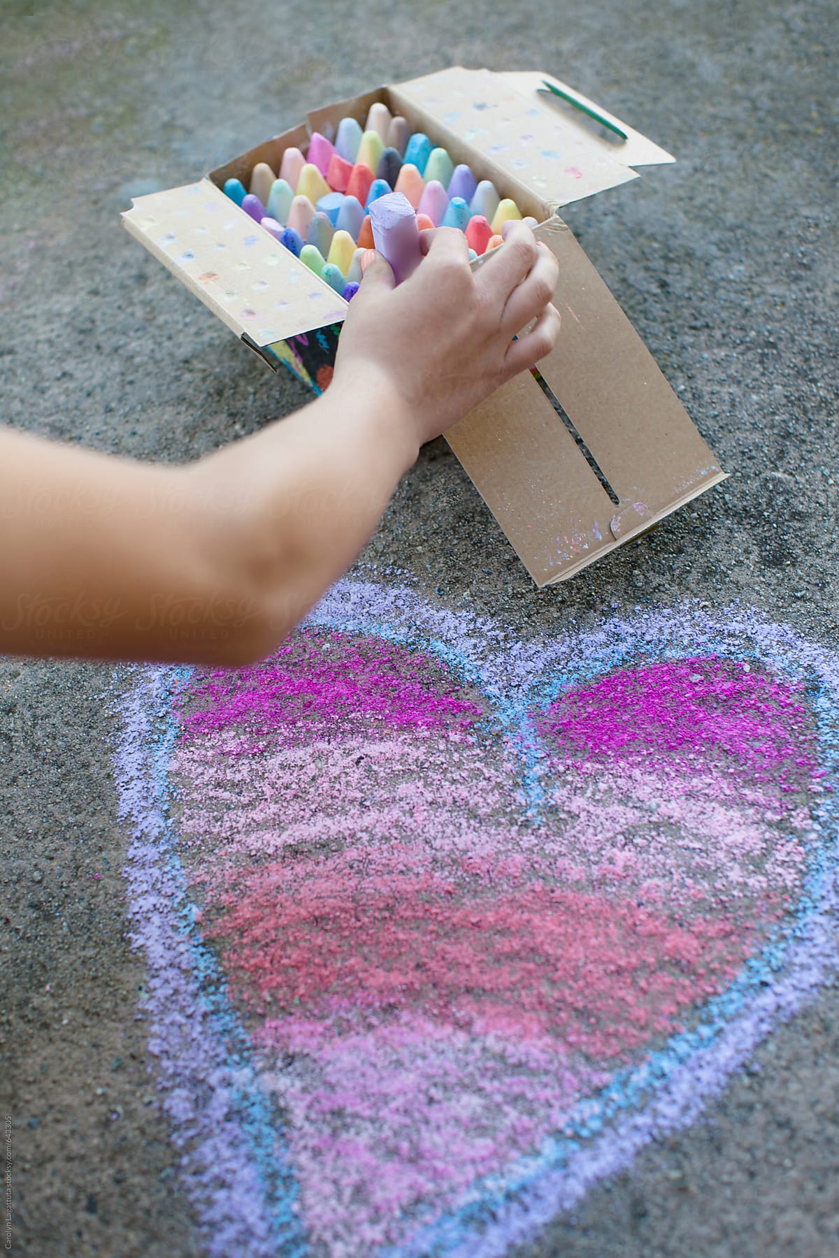 Young girl drawing a chalk heart on the pavement