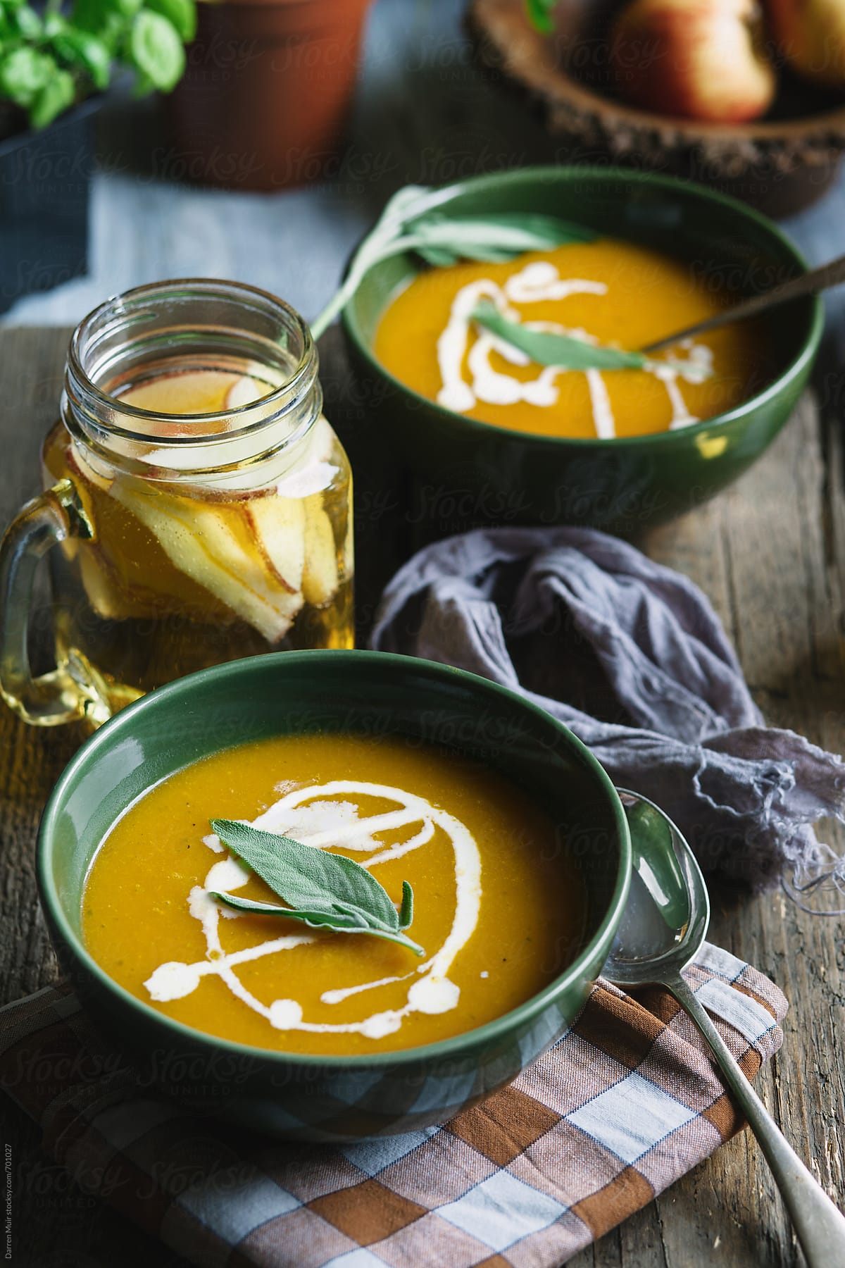 Two servings of butternut squash soup and a jug of cider on a table.