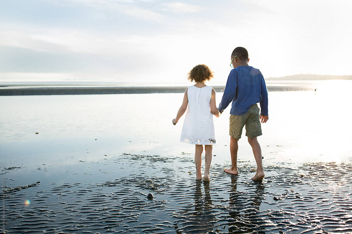 Cutebrother and sister hold hands on beach at low tide