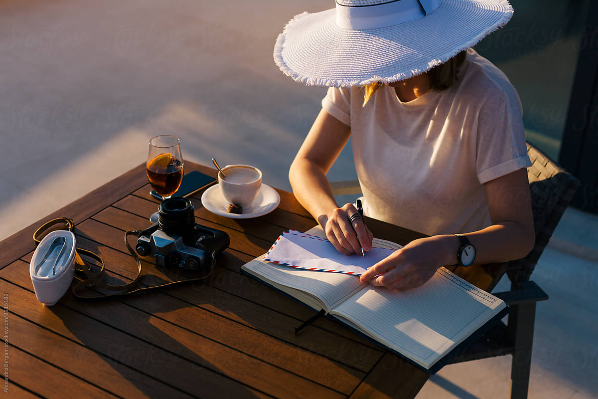Woman in white hat writes a letter in café at sunset