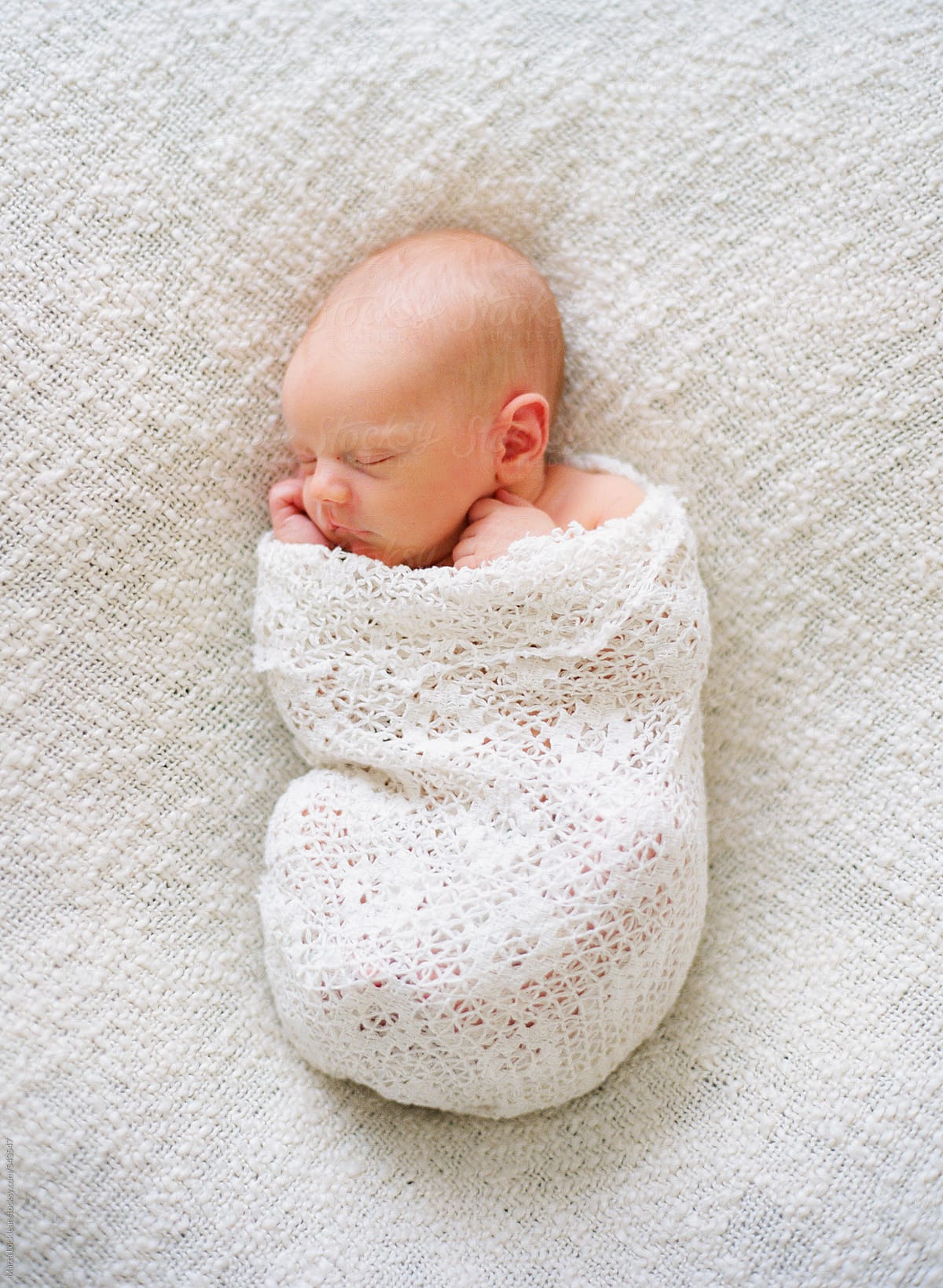 Newborn baby swaddled in a white blanket sleeping