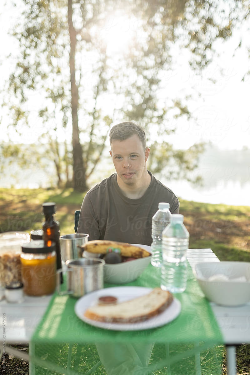 young man with down syndrome camping in nature having breakfast