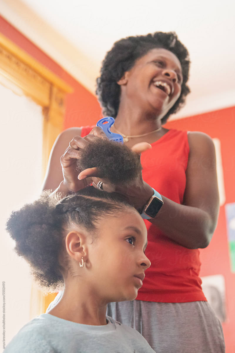 Mother combing her child\'s hair while watching tv