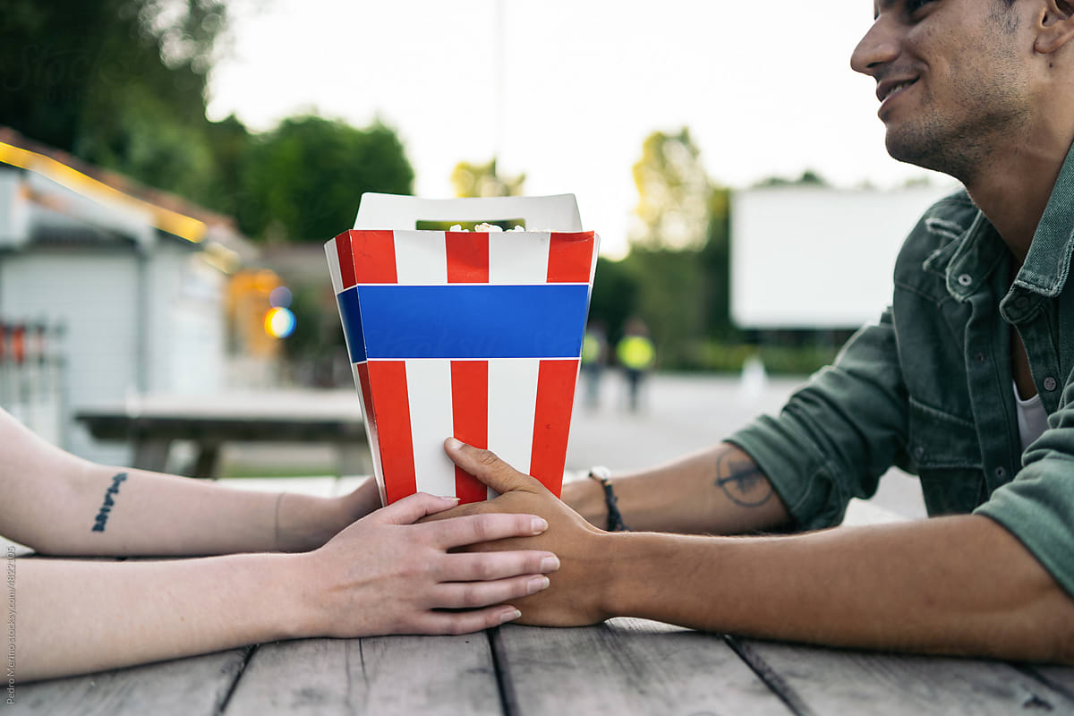 Close-up of a couple holding hands and sharing a bowl of popcorn