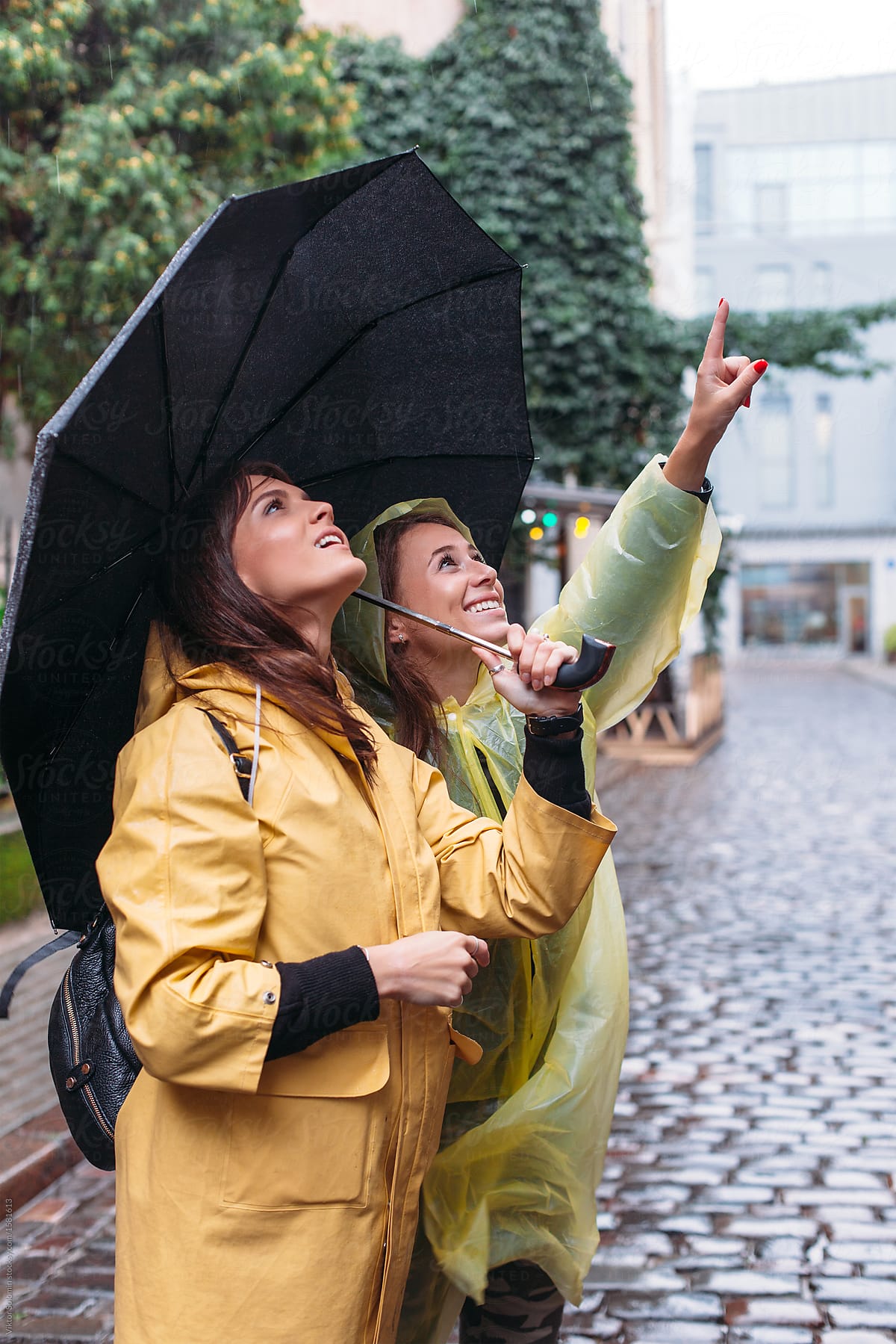 Pretty young smiling and happy brunette woman tourists are looking the city under the rain