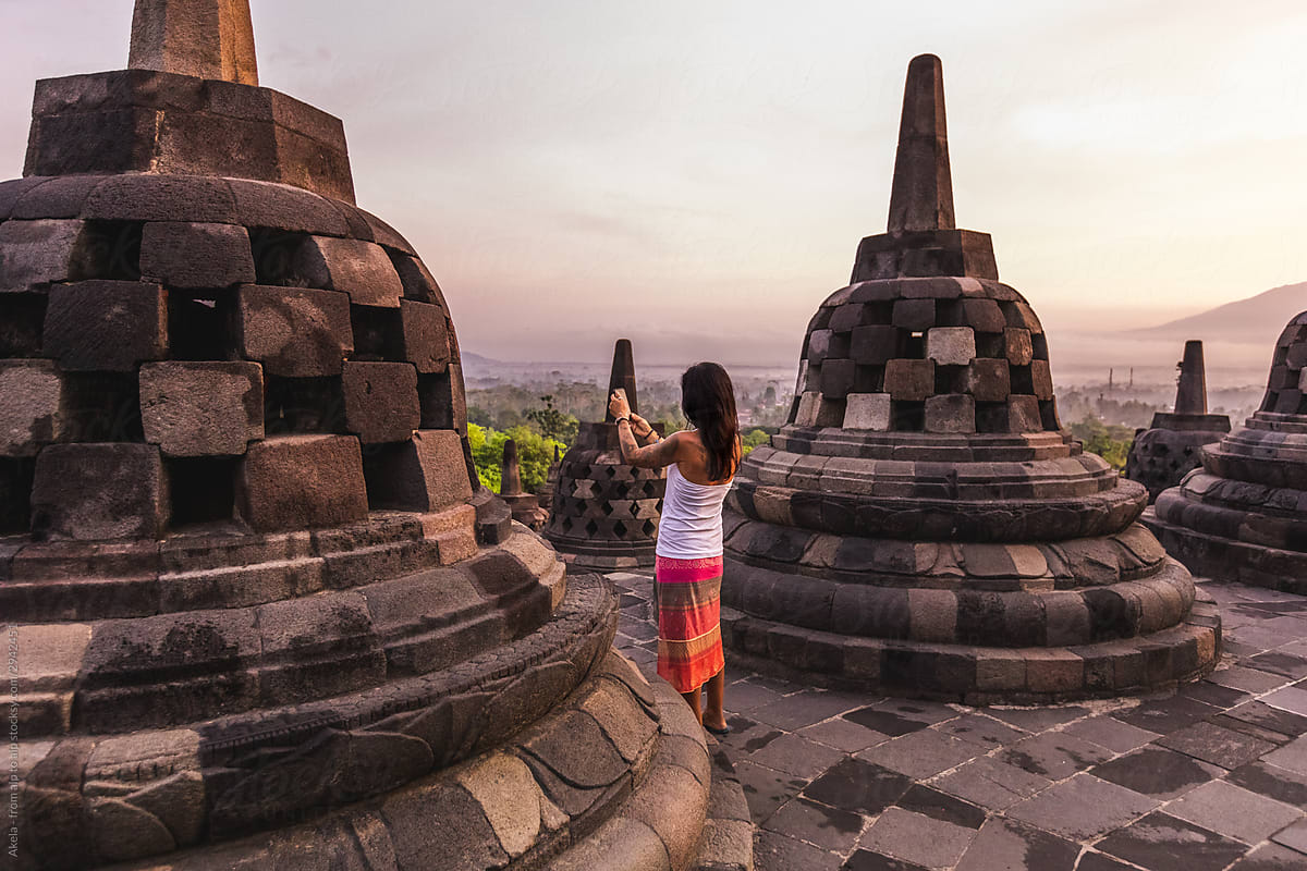 beautiful woman in colorful skirt taking a picture of buddhist temple at sunrise
