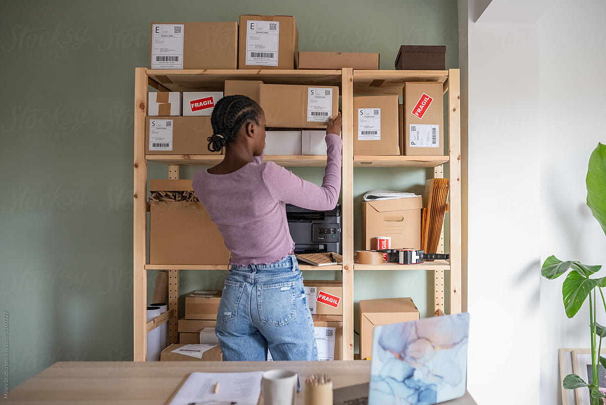 Black woman arranging boxes on wooden shelves in office