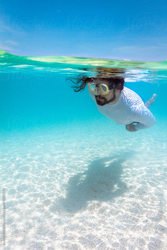 Man snorkeling underwater in tropics over the white sand
