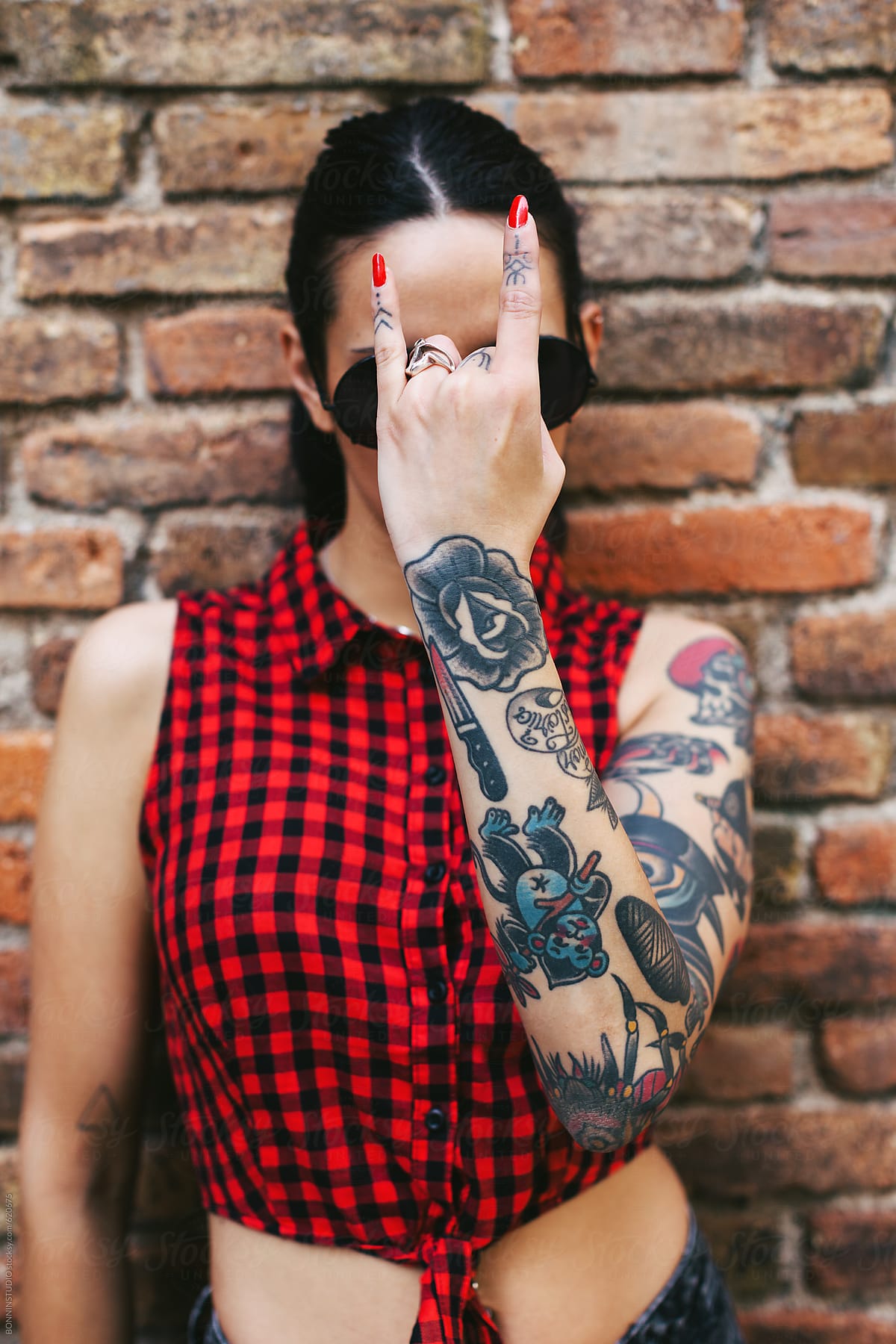 Young alternative woman with tattoos covering her face with a heavy metal sign.