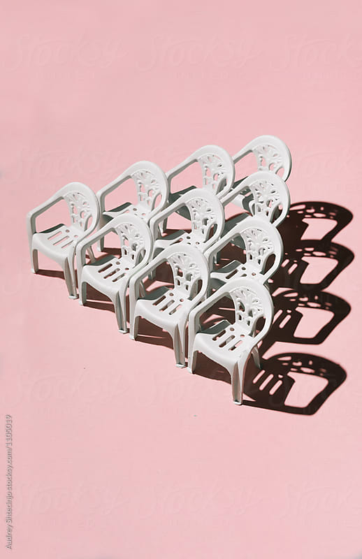 White chairs arranged in triangle formation on pink background.