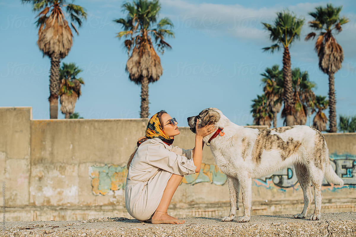 Woman talking to her dog with a wall and palm trees on background