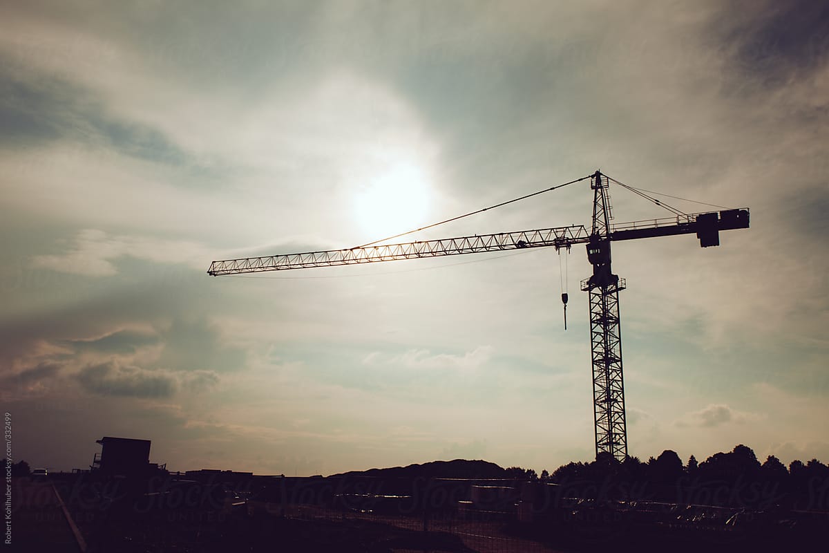 Industrial construction crane and building site silhouettes over sunny and cloudy sky