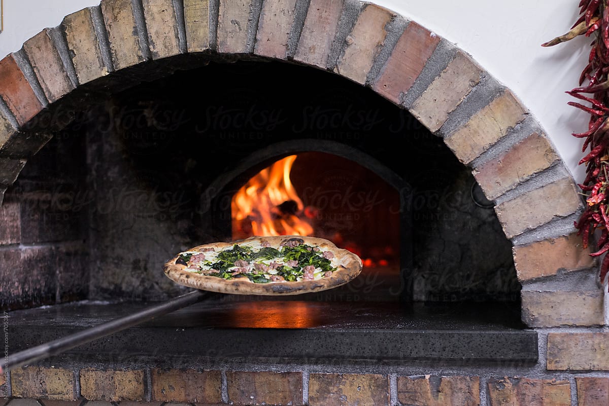 A pizza being put in to a wood fired oven for cooking