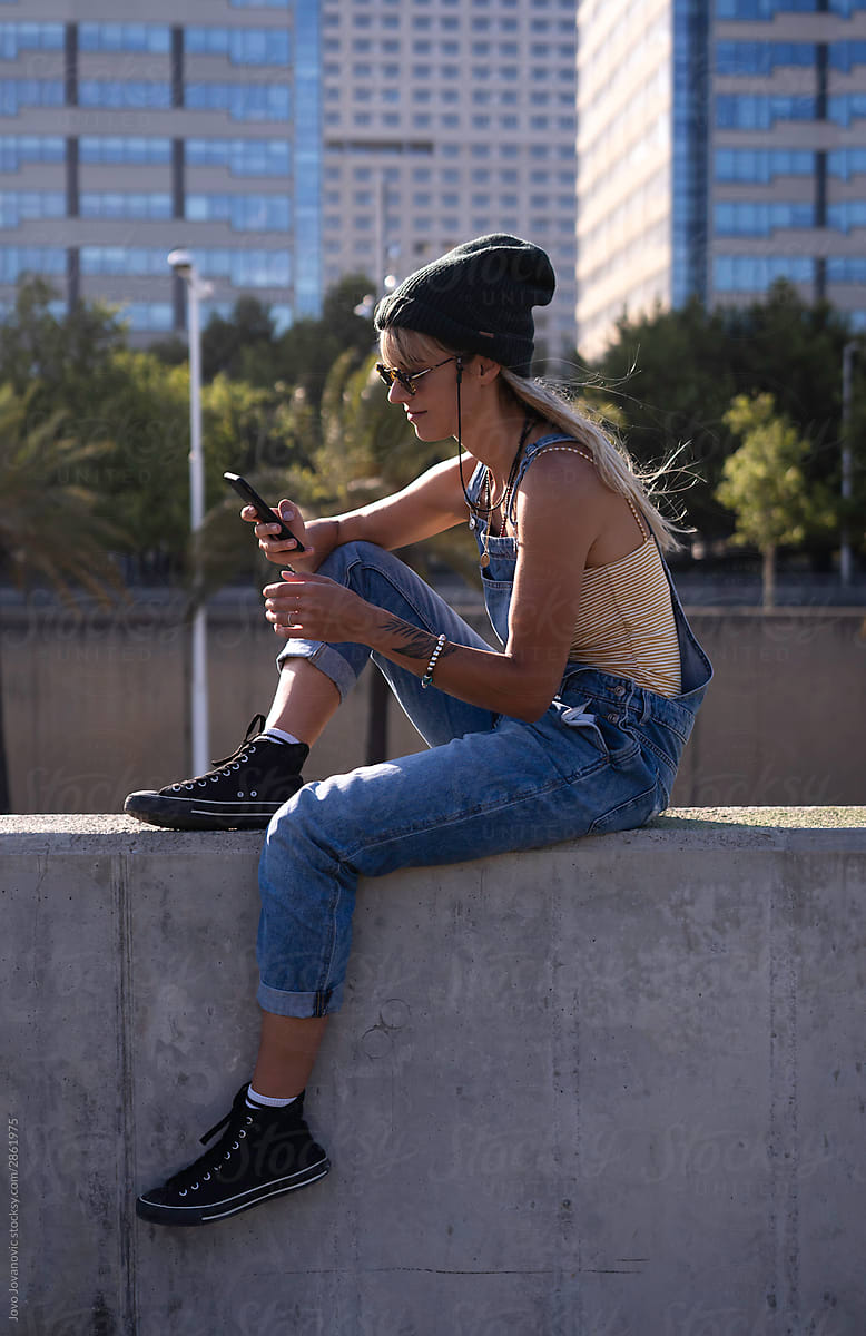 Fashionable woman relaxing outside while checking messages on phone