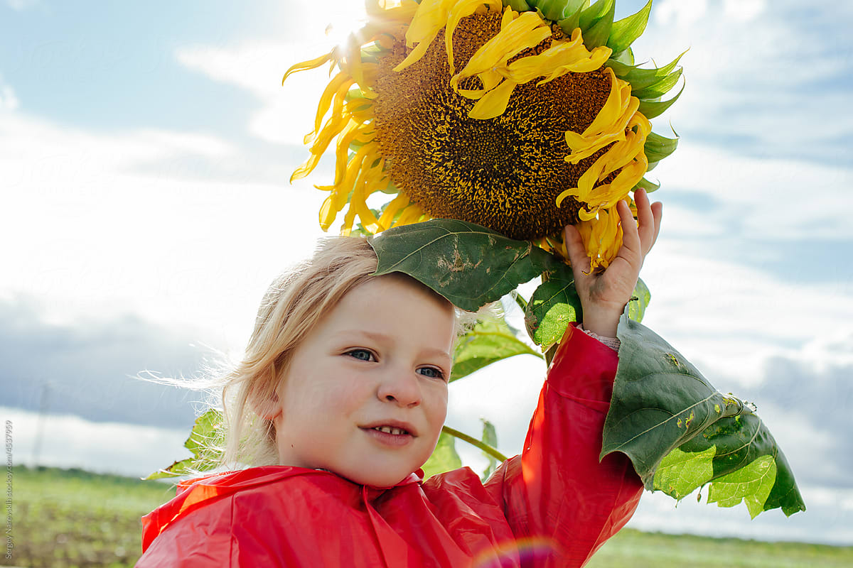 Child near sunflower against cloudy sky