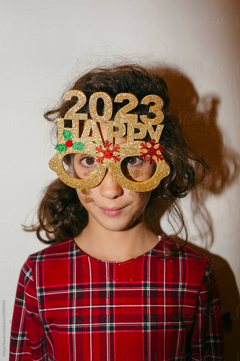 Kid making funny faces with Happy 2023 party glasses over white wall