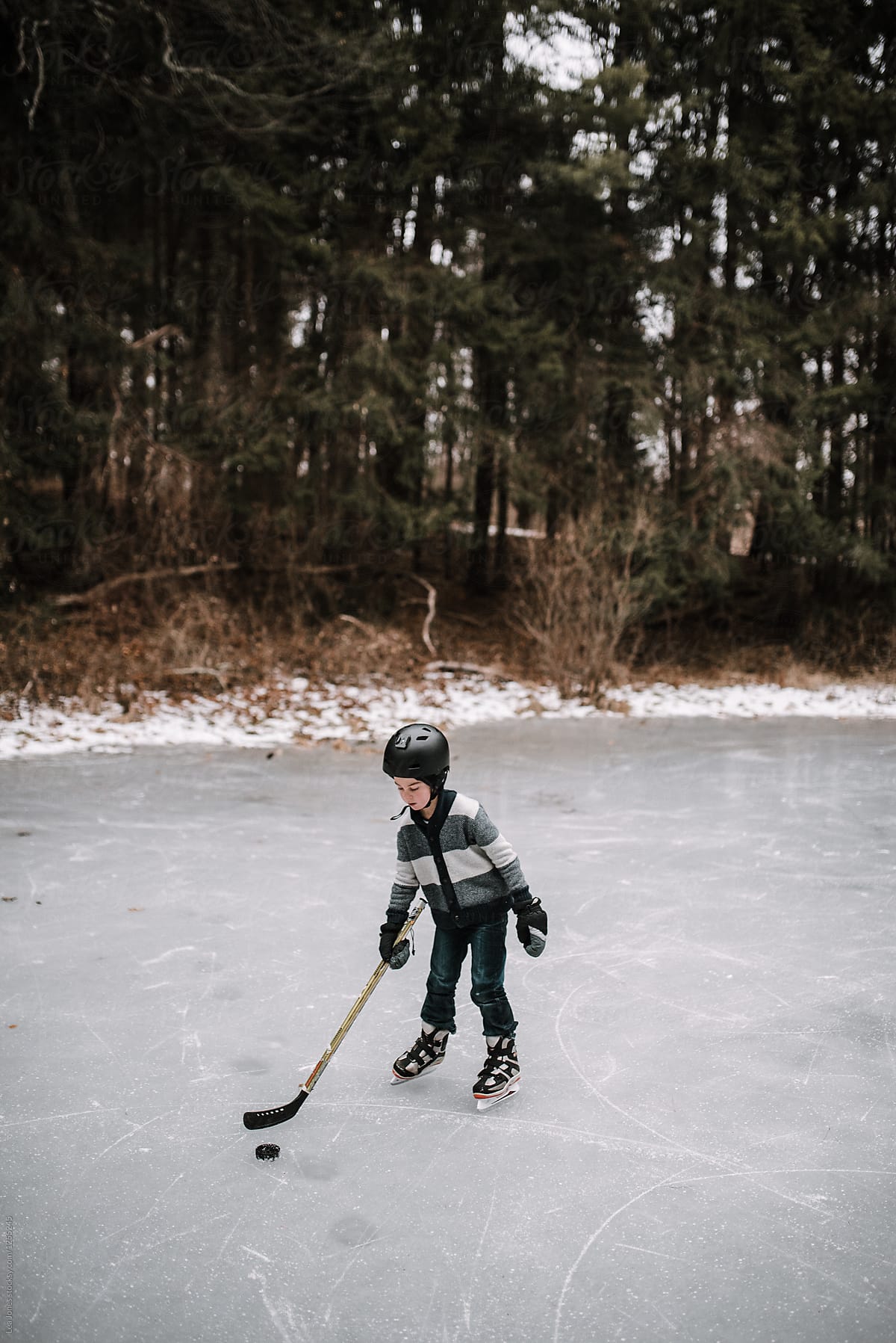 little boy playing hockey on a pond