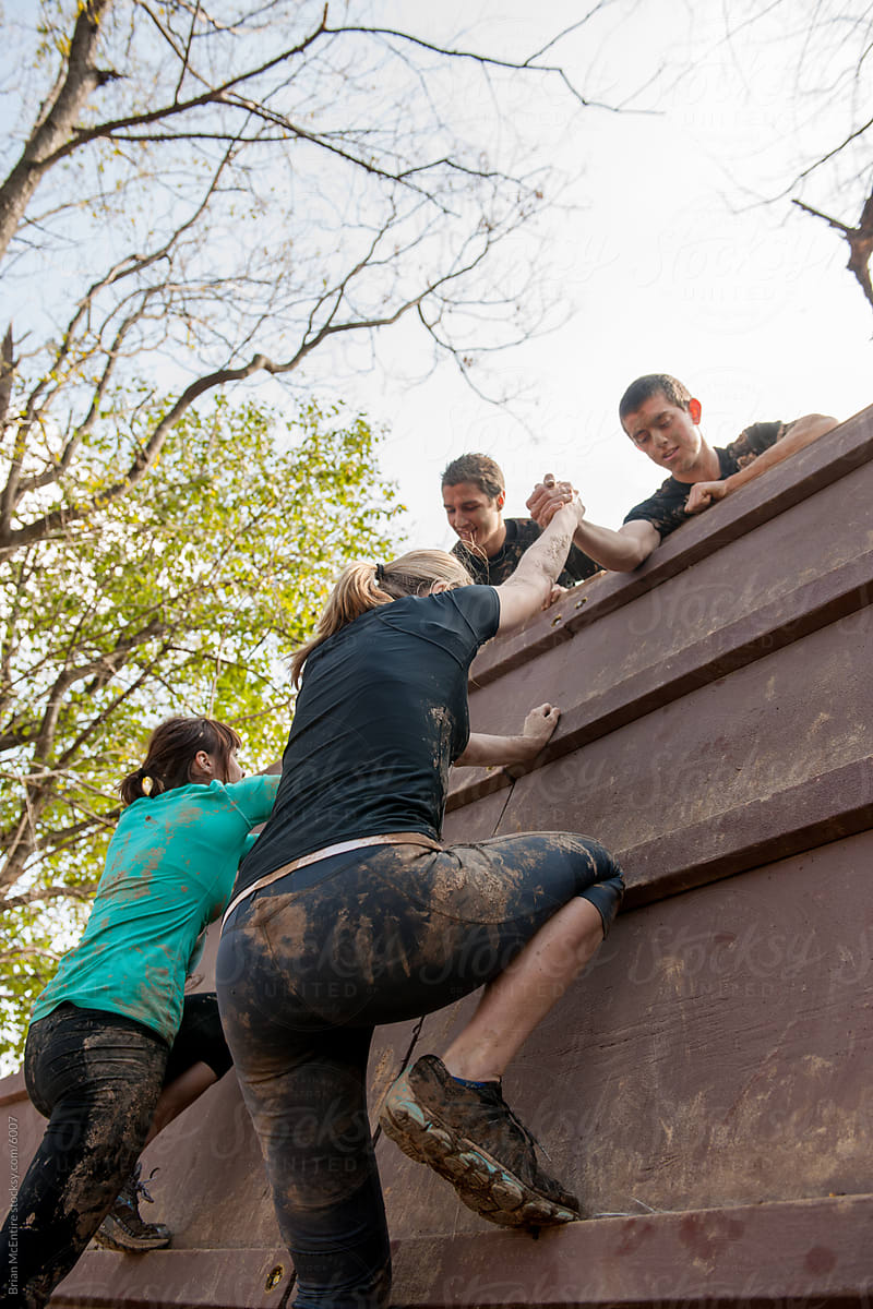 Competitors Help Each Other Over Climbing Obstacle on Mud Run