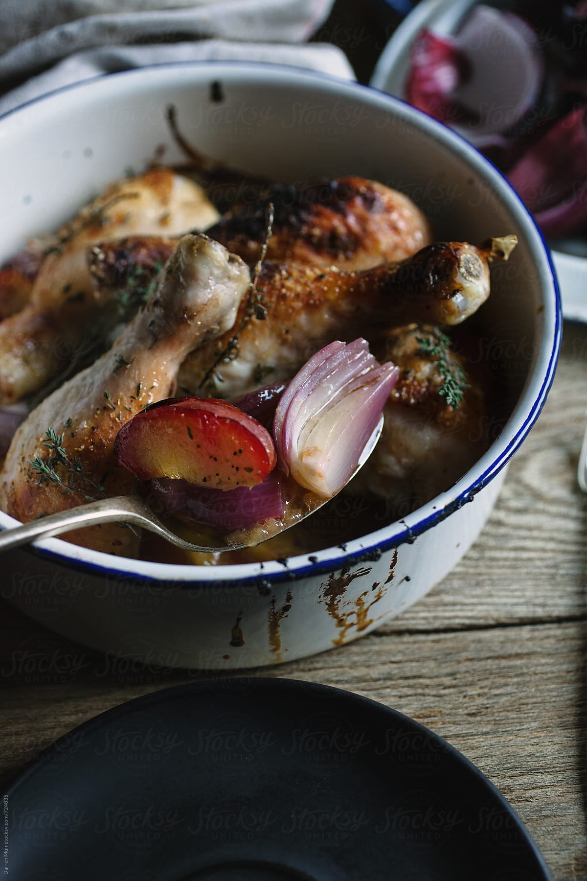 Rustic meal of chicken with red onion and plums in a pot.