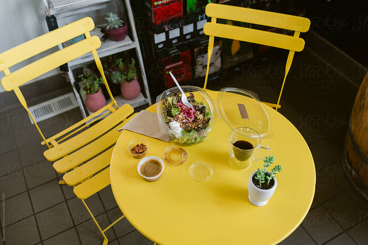 Round table and yellow chairs with salad and coffee
