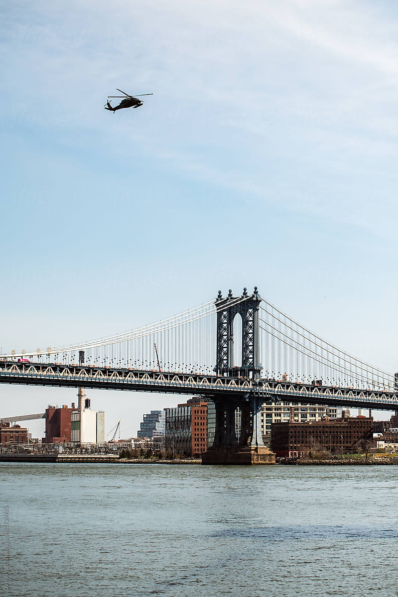 Helicopter over Manhattan Bridge with clear blue sky.