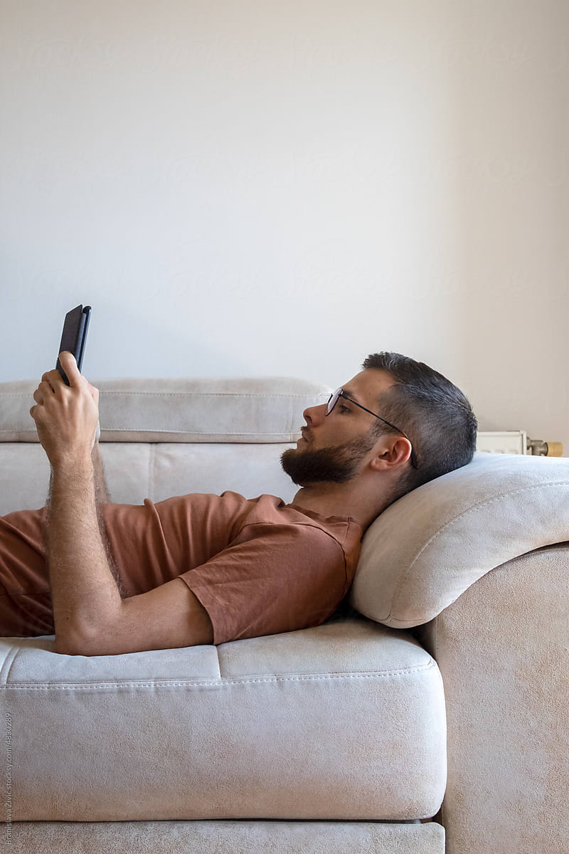 Young male model reading kindle and lounging on the sofa