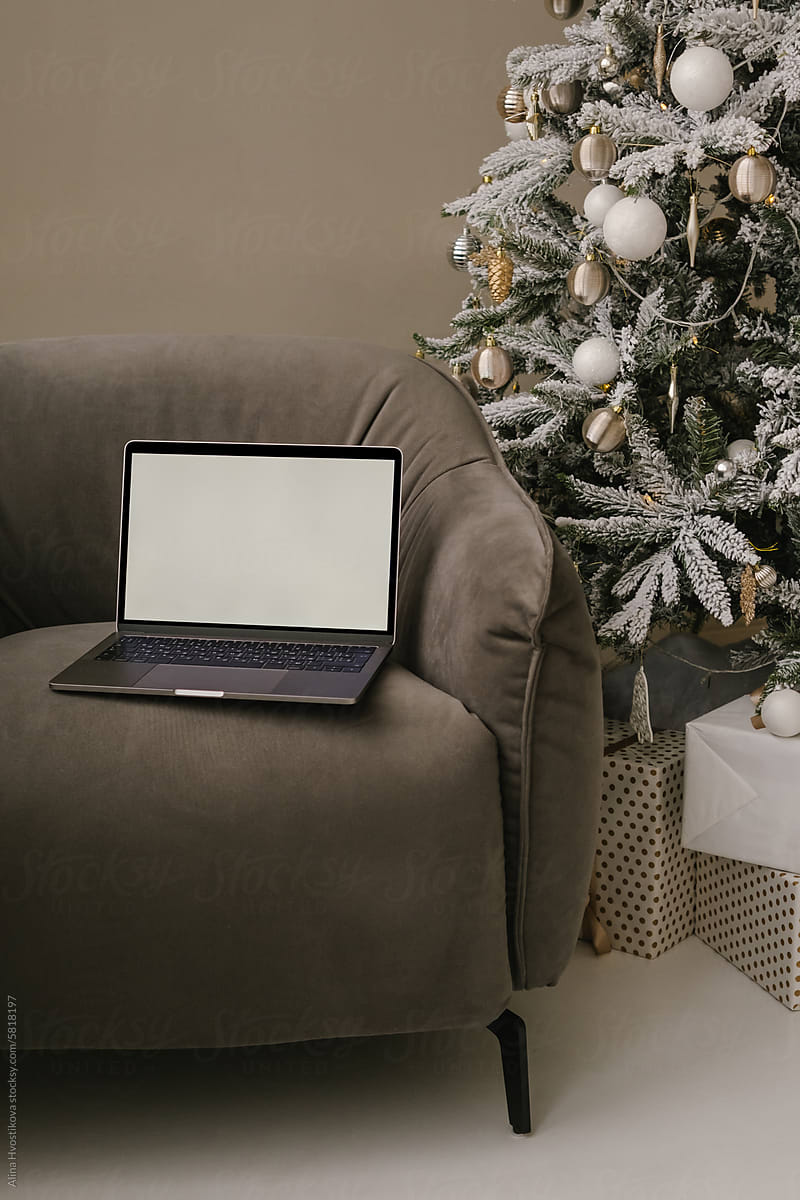 Laptop with blank screen placed on sofa near Christmas decorations