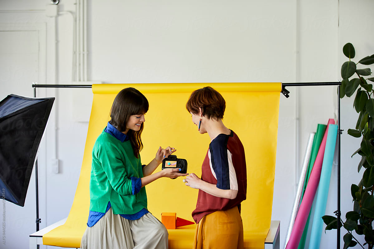Designer Showing Camera To Colleague By Backdrop