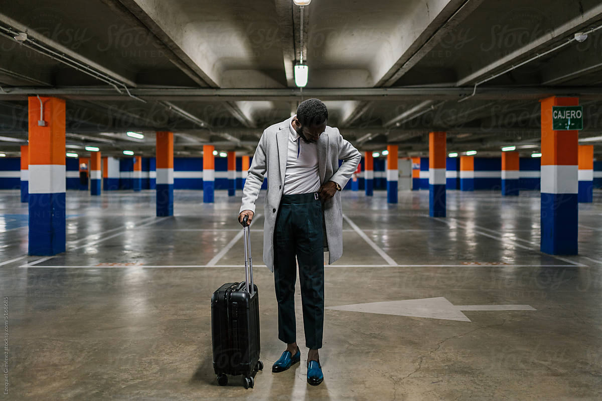 Trendy black man with suitcase in parking