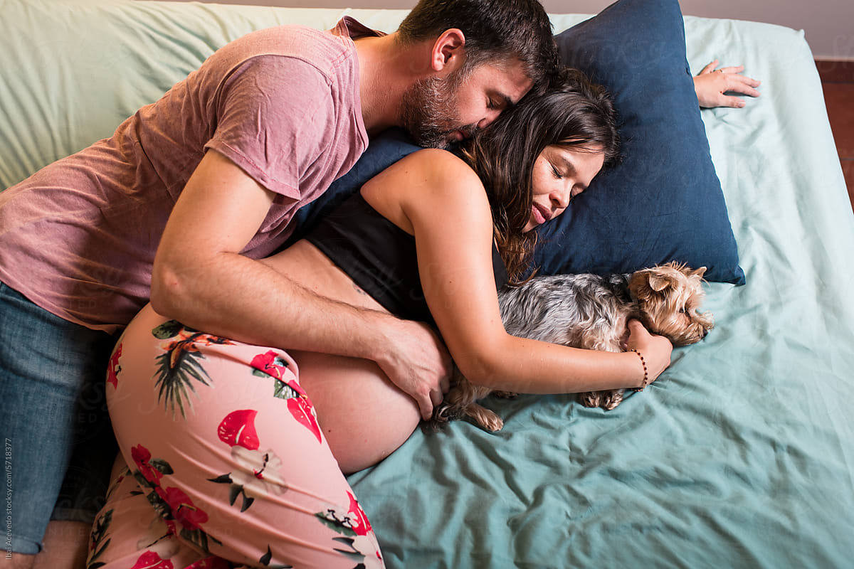 Pregnant couple sleeping with little dog on bed