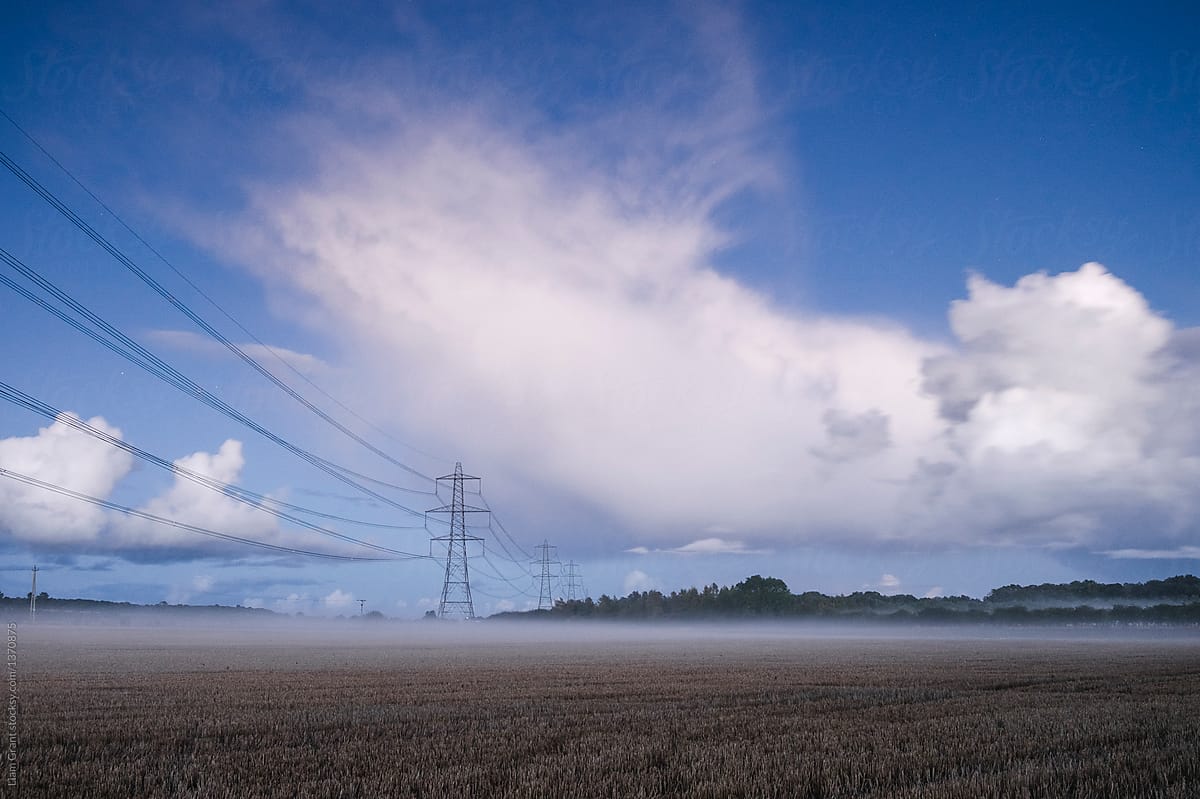 Electricity pylon and rising fog in a field at night. Norfolk, U