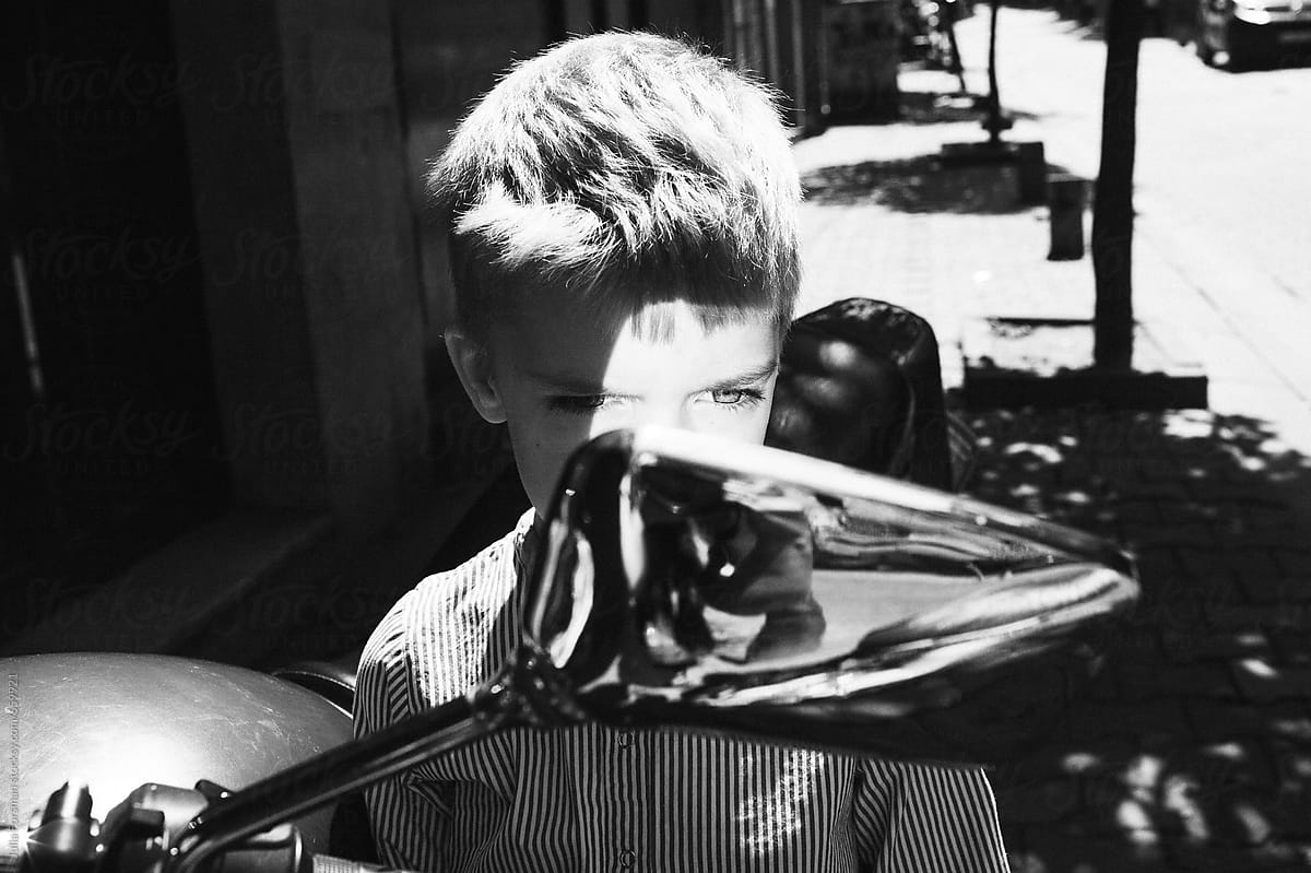 Black and white of light haired boy child looking into a moped mirror.