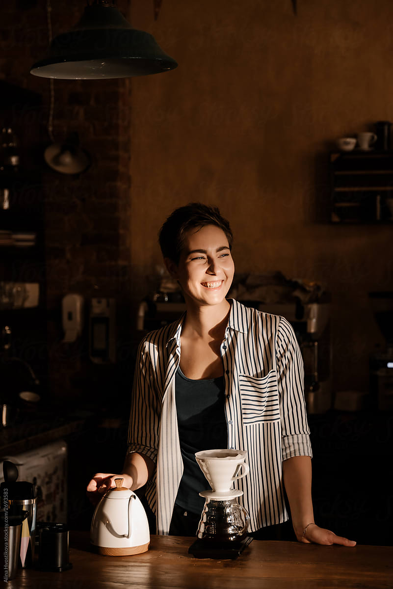 Positivity barista holding glasses kettle and smiling.