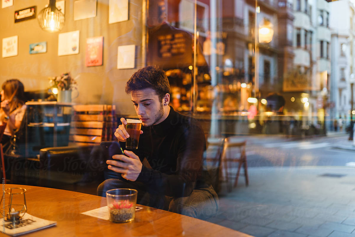 Thoughtful man with smartphone drinking beer in pub