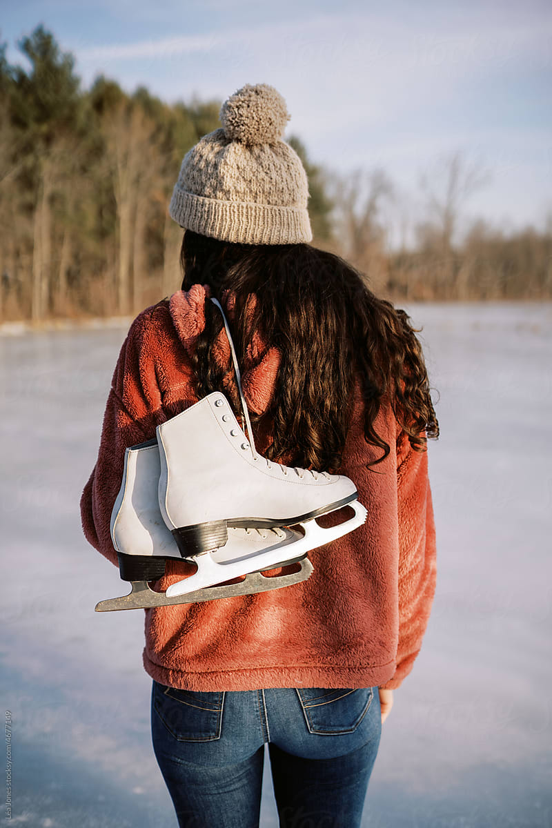 young woman by lake holding skates