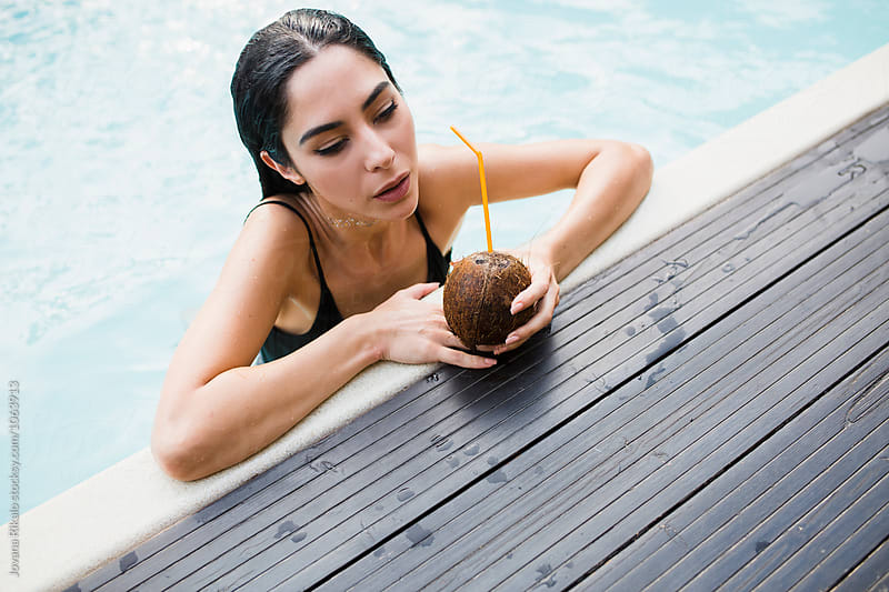 Young woman drinking coconut by the pool