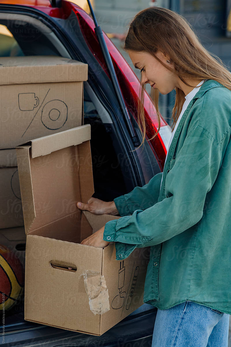 Young woman packing cardboard box in car trunk