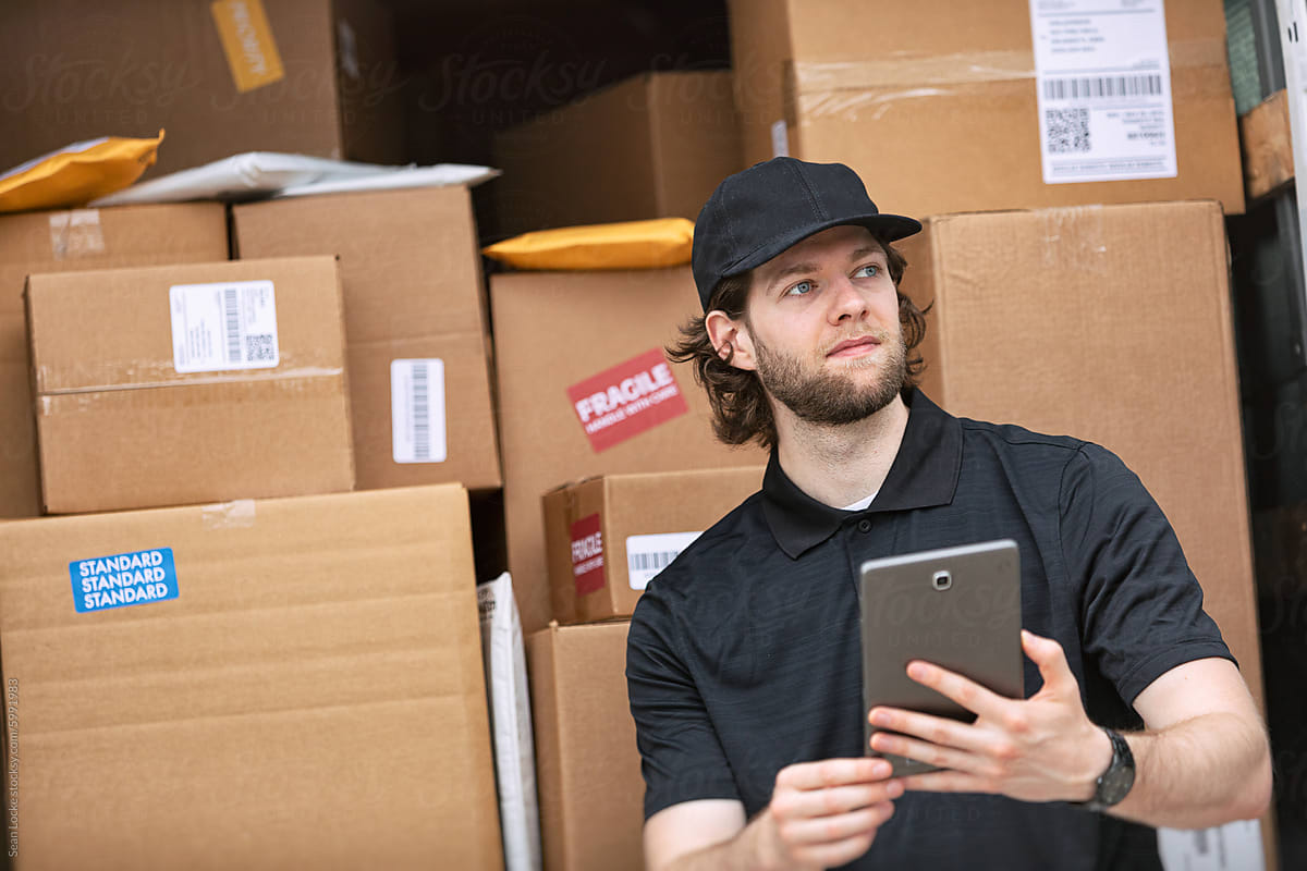 Shipment: Man Sits On Bumper To Relax While Checking Tablet