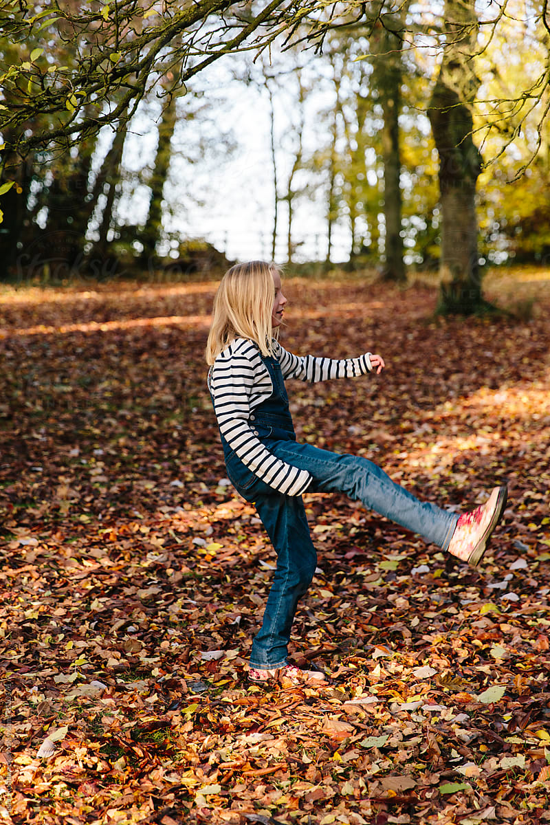 Girl Outdoors Kicking Fallen Leaves By Helen Rushbrook