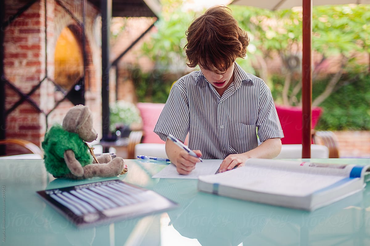 Boy Sitting At An Outside Table Doing His Homework After School by Stocksy  Contributor Angela Lumsden - Stocksy